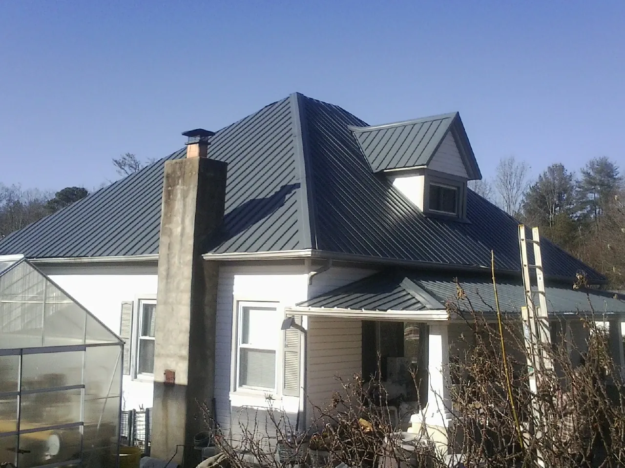 Dark blue standing seam metal roof on a white farmhouse with dormer — Slate & Tile Roof Repair by Roofing Brothers in Ronco