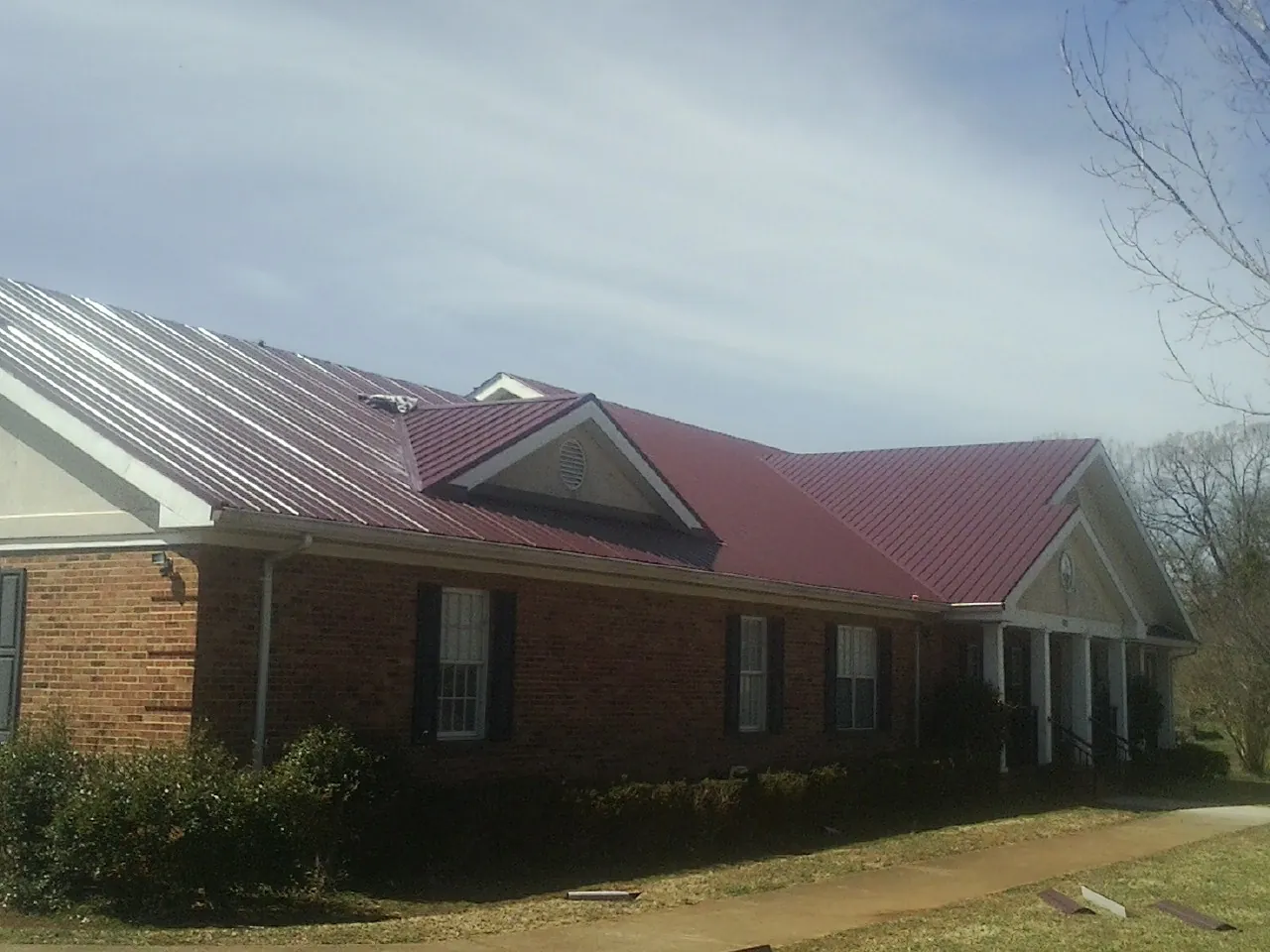Red metal roof with gabled entries on a long brick building, from a Hail Damage Roof Repair job in Ronco