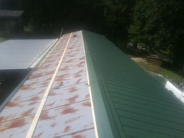 Old rusted panels beside newly installed green metal roofing — Wind Damage Roof Repair by Roofing Brothers in Ronco