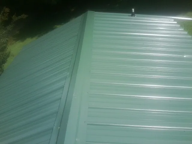 New green metal panels meeting at the ridge of a roof — Flat Roof Repair work by our crew in Ronco