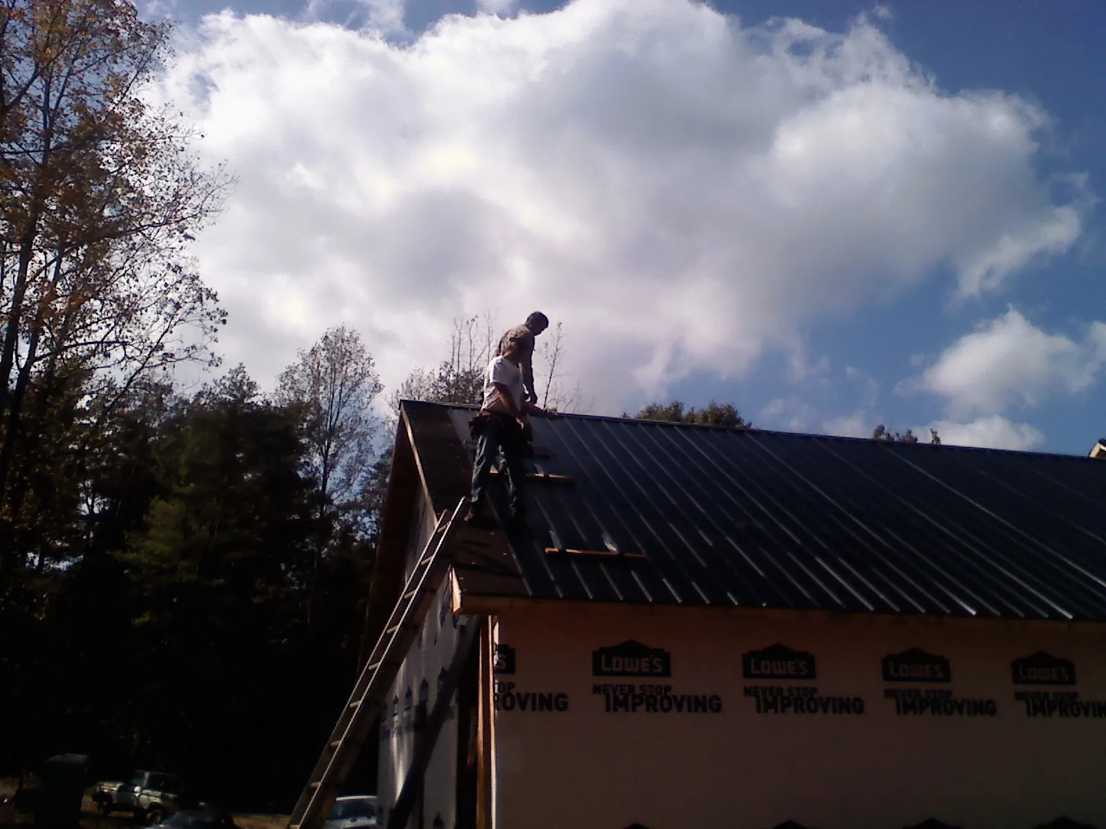 Roofer fastening dark metal panels high against a cloudy sky, from a Roof Inspection job in Ronco