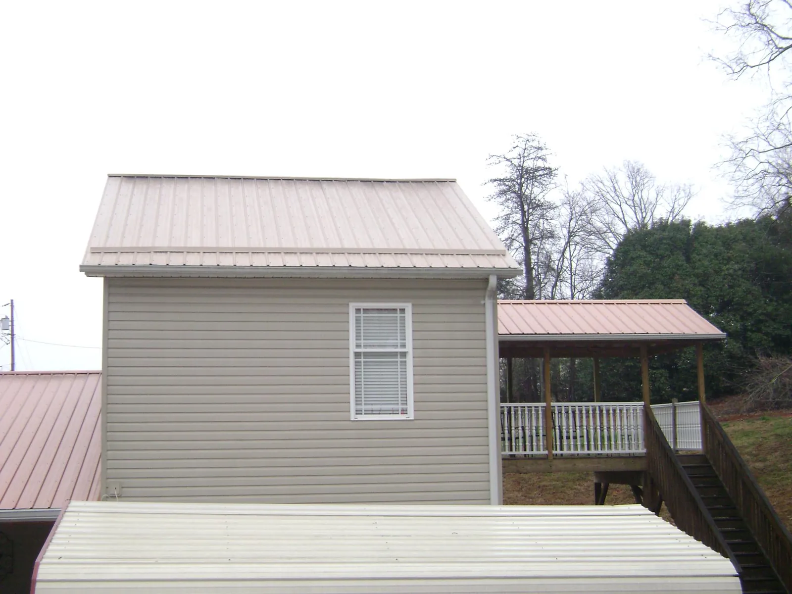 Tan metal roofs on a two story addition and attached porch, from a Roof Replacement job in Ronco